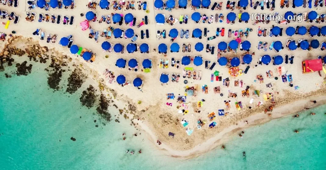Aerial View of a Sun-Drenched Beach Paradise Top-down aerial view of a crowded tropical beach with clear water and blue umbrellas.